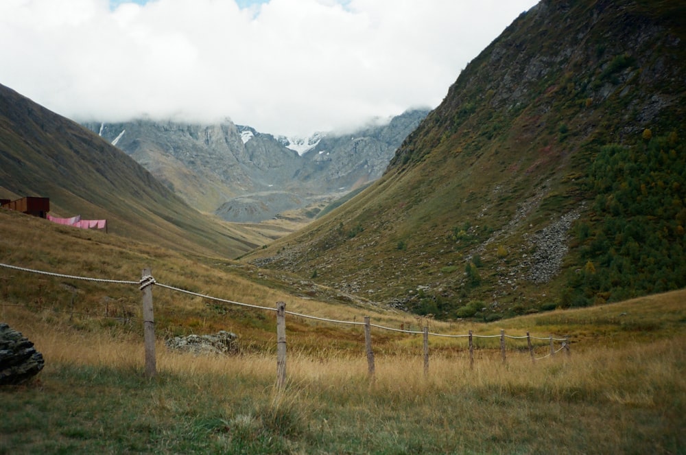 a grassy field with a fence and mountains in the background