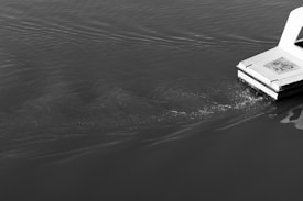 A floating platform extends into gently rippling water with a small splash surrounding its edge. The surface is calm, with the reflection of light providing contrast in the monochrome scene.