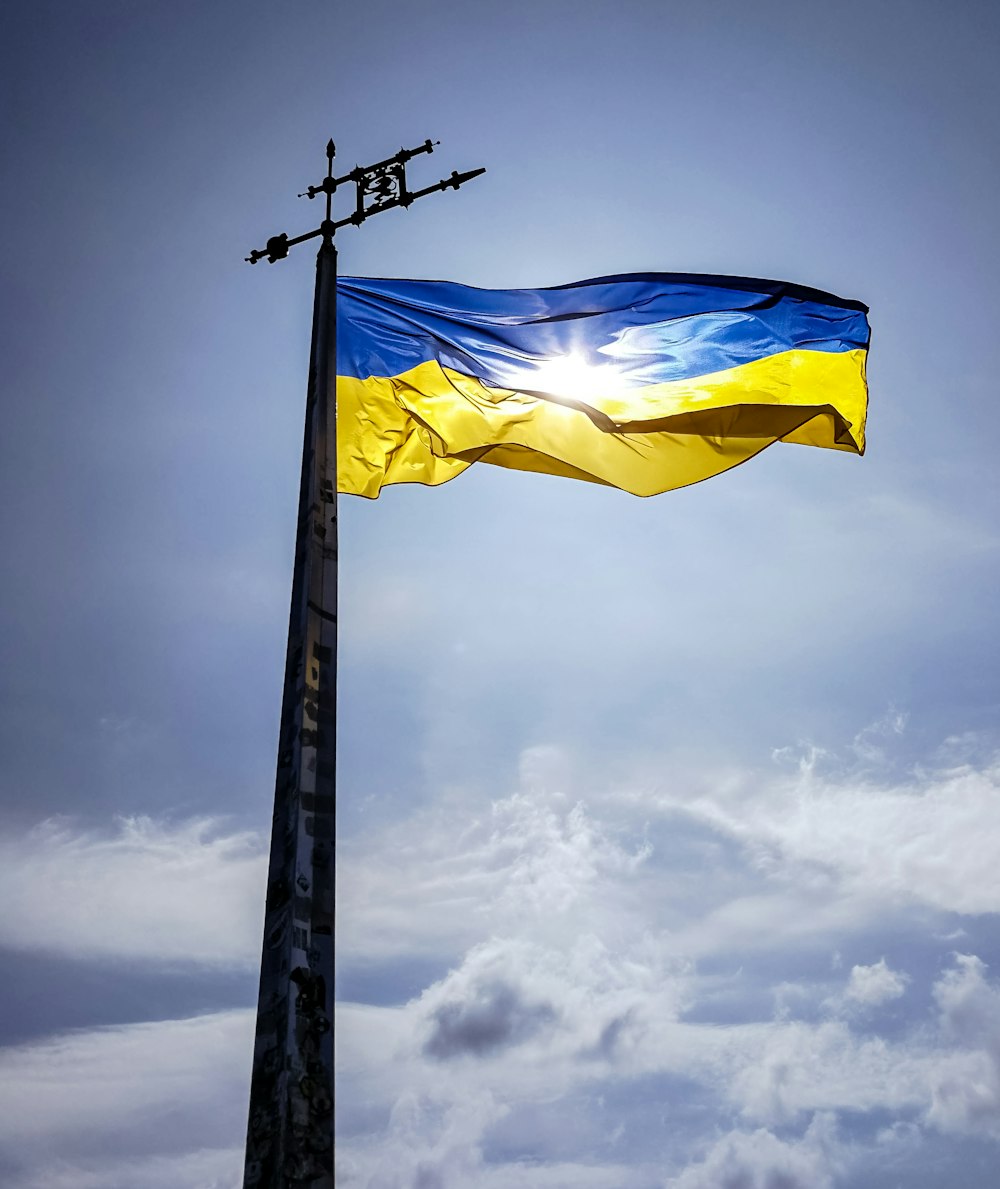 a blue and yellow flag flying on top of a tall pole
