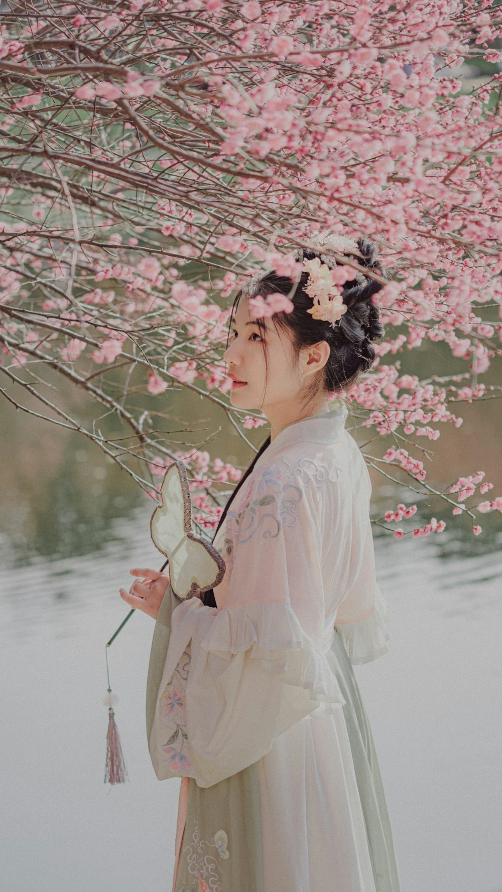 a woman in a white dress under a tree with pink flowers