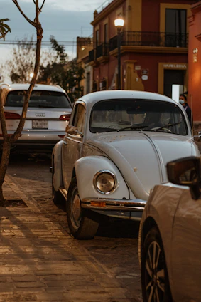 A classic vintage Volkswagen Beetle parked on a cobblestone street with sunlight casting warm shadows.