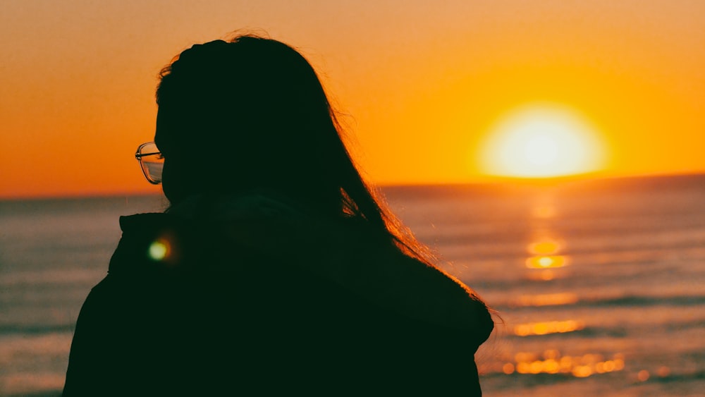 uma mulher olhando para o oceano ao pôr do sol