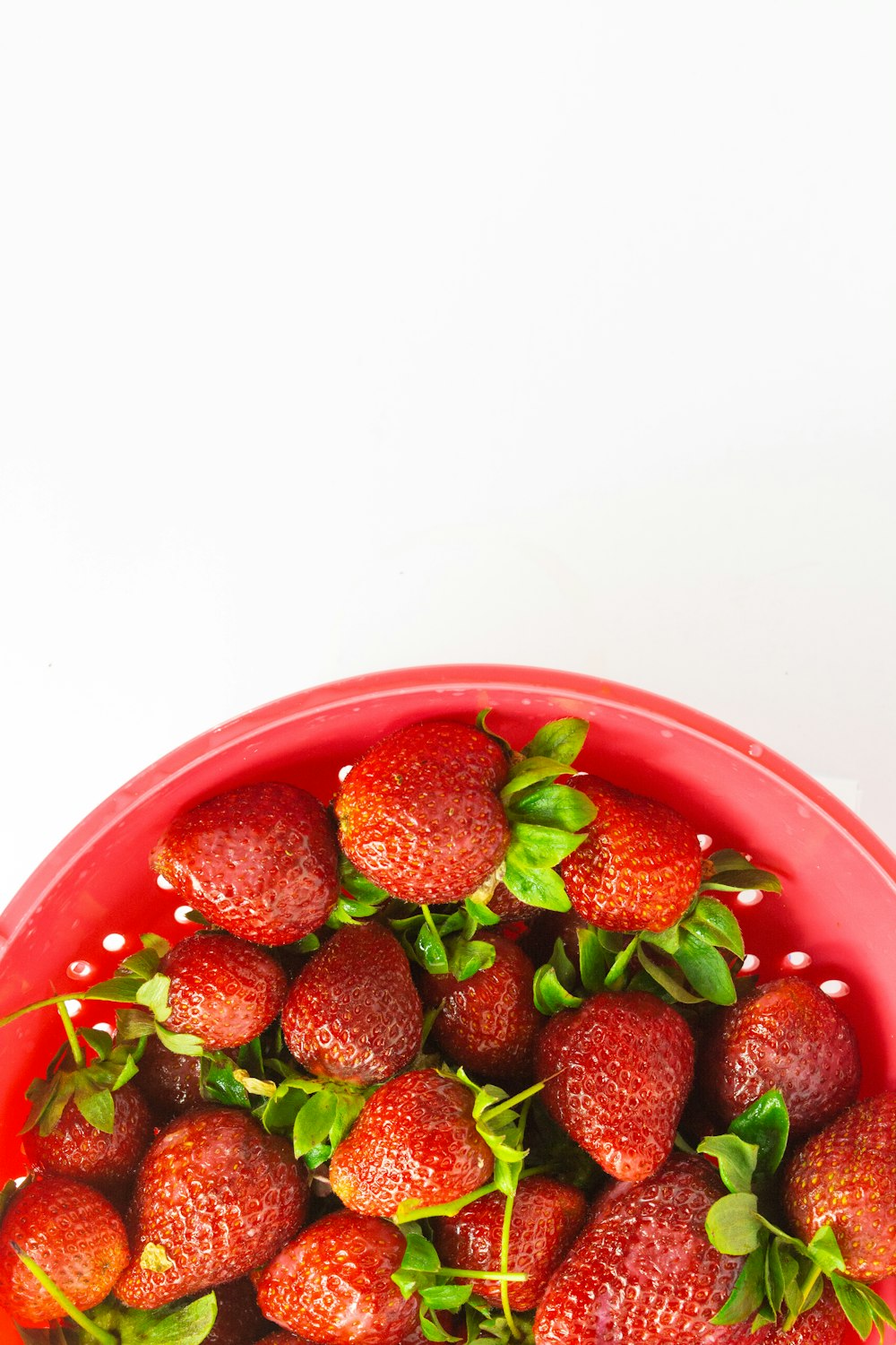 a red bowl filled with lots of ripe strawberries