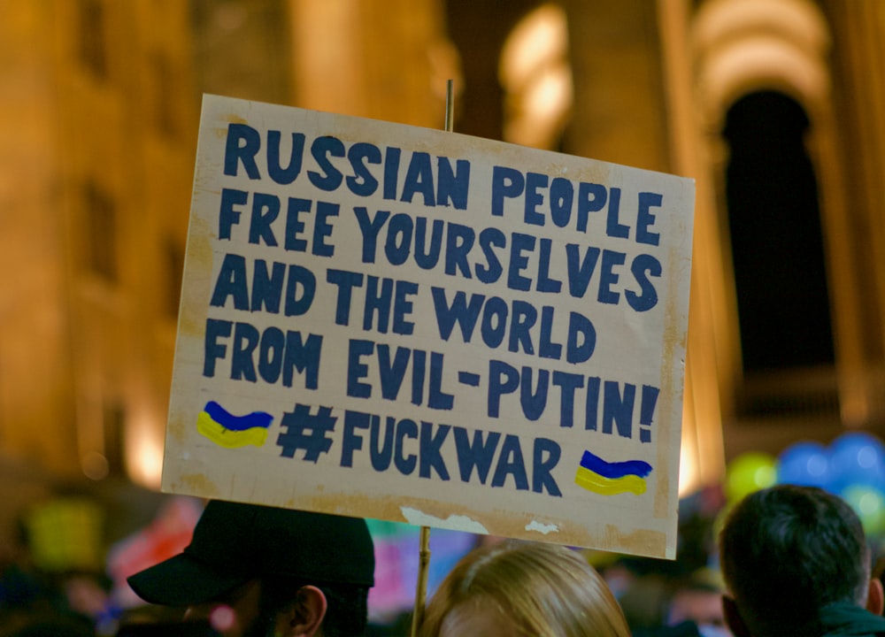 a man holding a sign that says russian people free themselves and the world from evil