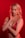 A person with blonde hair poses against a vibrant red background. They are wearing red lingerie and have a calm, confident expression. The lighting emphasizes the warm tones, creating a dramatic effect.