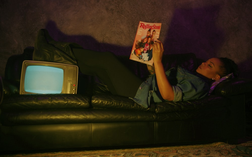 a woman laying on a couch reading a book