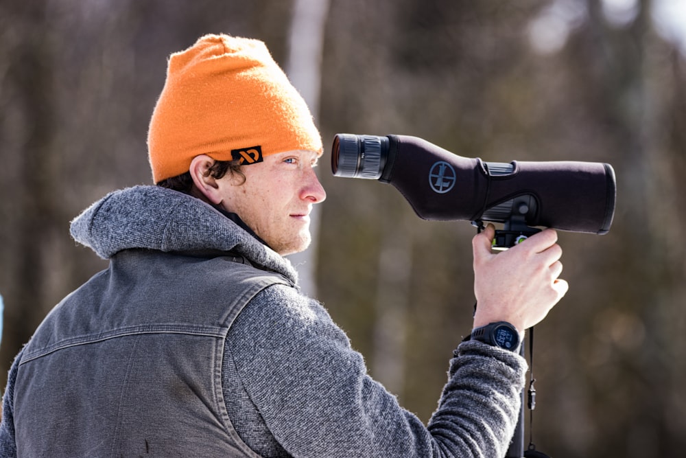 a man wearing a beanie looking through a telescope