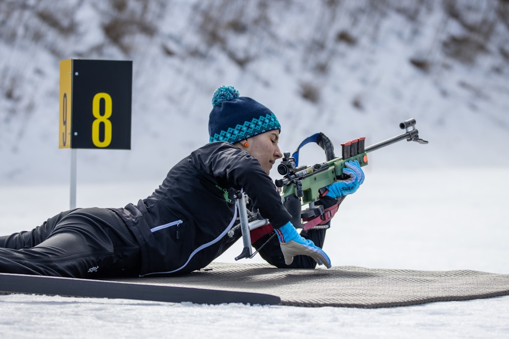 a person laying on a snow covered ground with a rifle