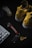 A pair of yellow sneakers with a distinctive logo on a dark background, accompanied by a gaming mouse on the left side and a desktop keyboard partially visible at the bottom. A set of car keys with a keychain featuring miniature sneaker design and branding are placed in the center.