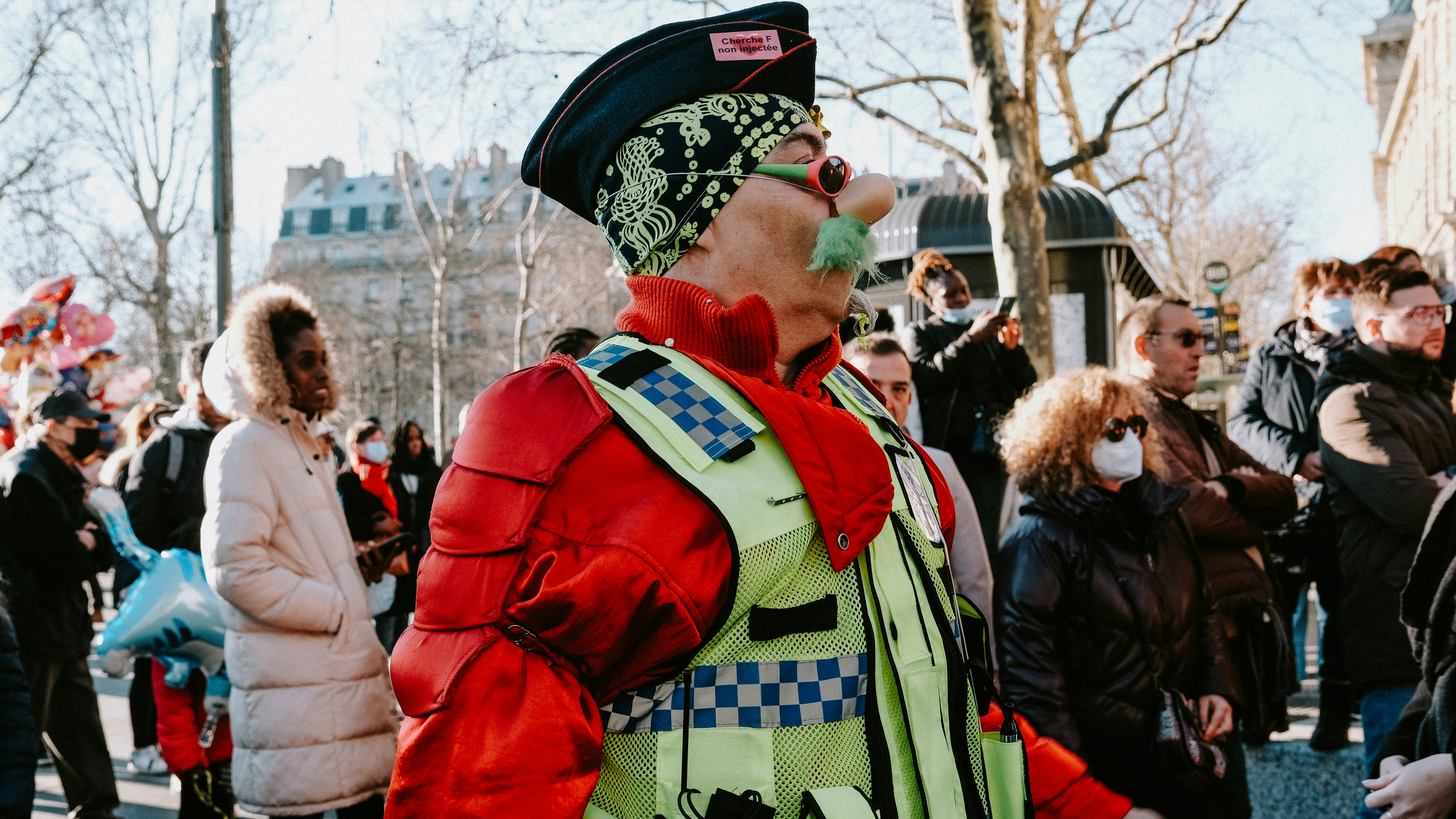 a man in a red jacket and green vest standing in front of a crowd