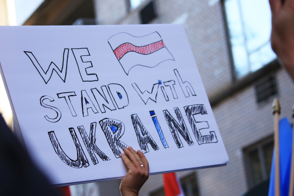 a person holding a sign that says we stand with ukraine