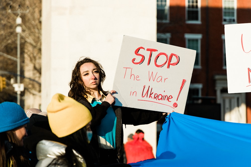 a woman holding a sign that says stop the war in ukraine
