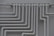A series of parallel white pipes with multiple bends and joints is arranged on a light gray wall. The pipes display slight rust and wear in certain areas, indicating exposure to elements over time.