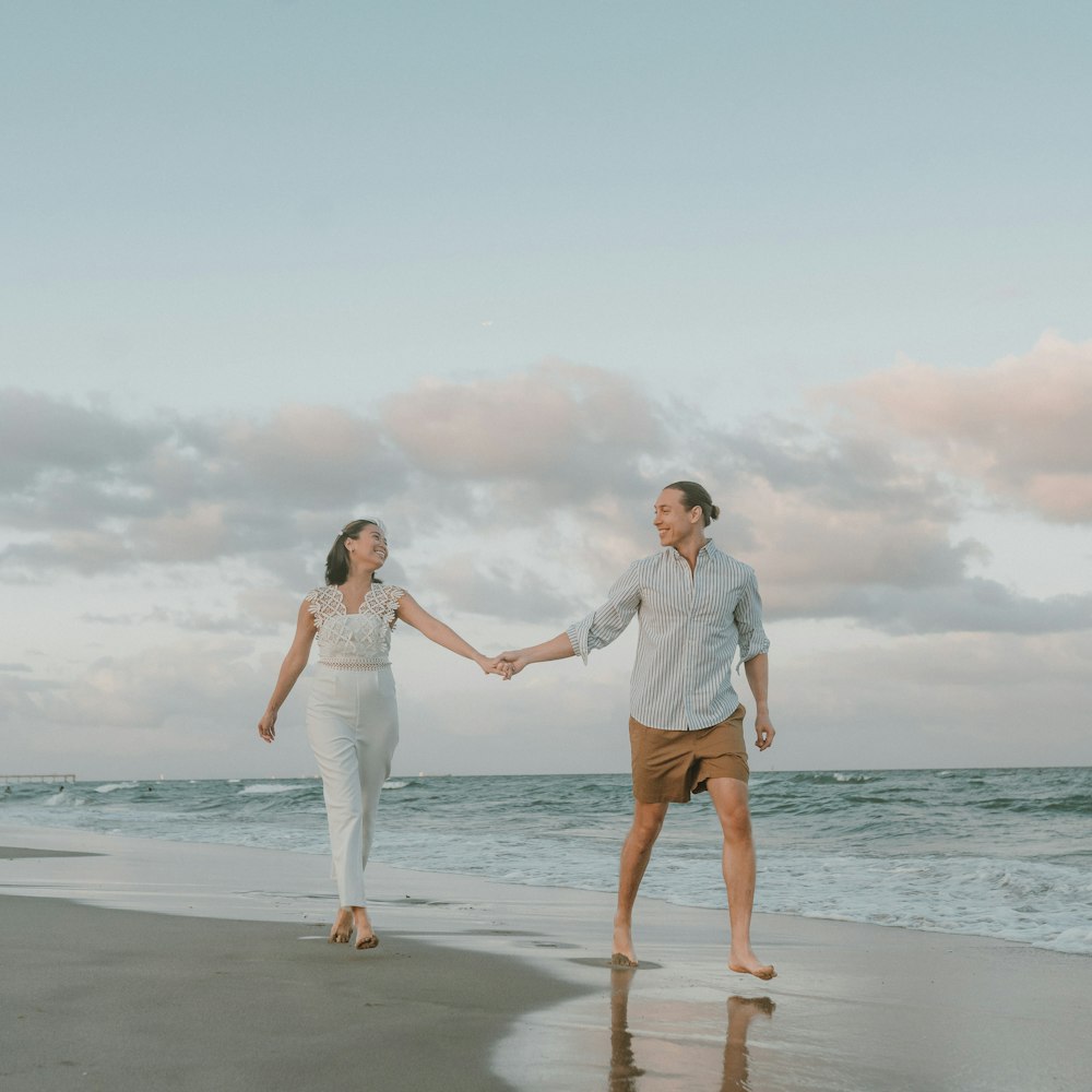 a man and woman holding hands while walking on the beach