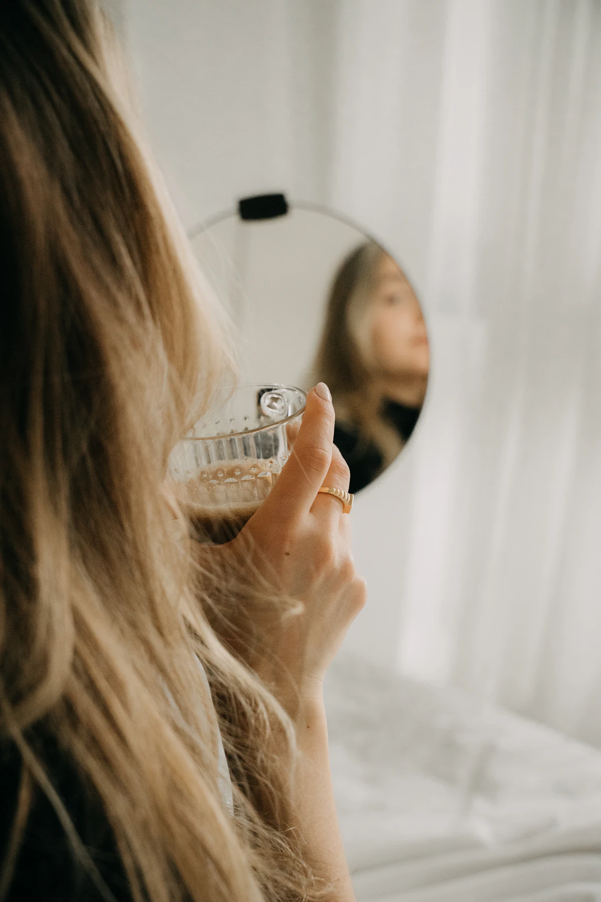 Woman gently massaging her scalp with fingertips while looking in a mirror