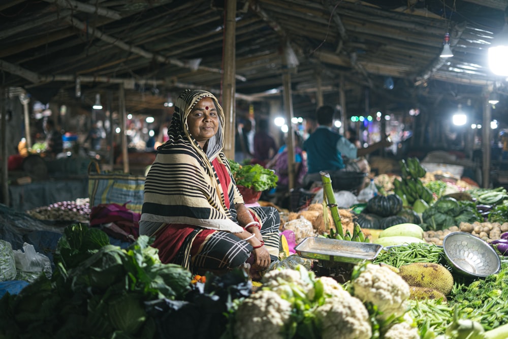 a woman sitting in front of a pile of vegetables