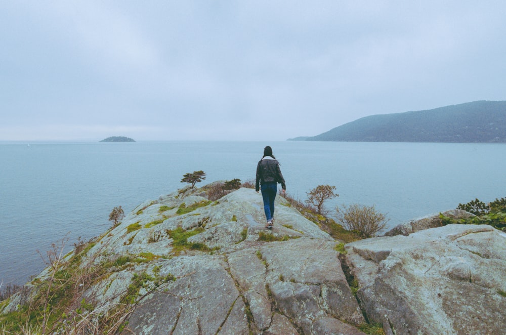 a person standing on top of a large rock next to a body of water