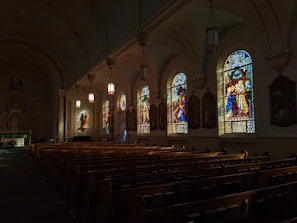 Softly lit chapel interior with stained glass windows casting colorful light on wooden pews.