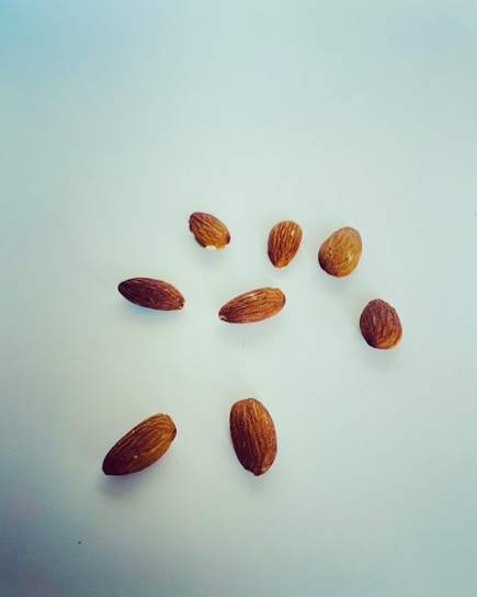 Several raw almonds scattered on a clean, white surface. The almonds have a light brown, textured shell.