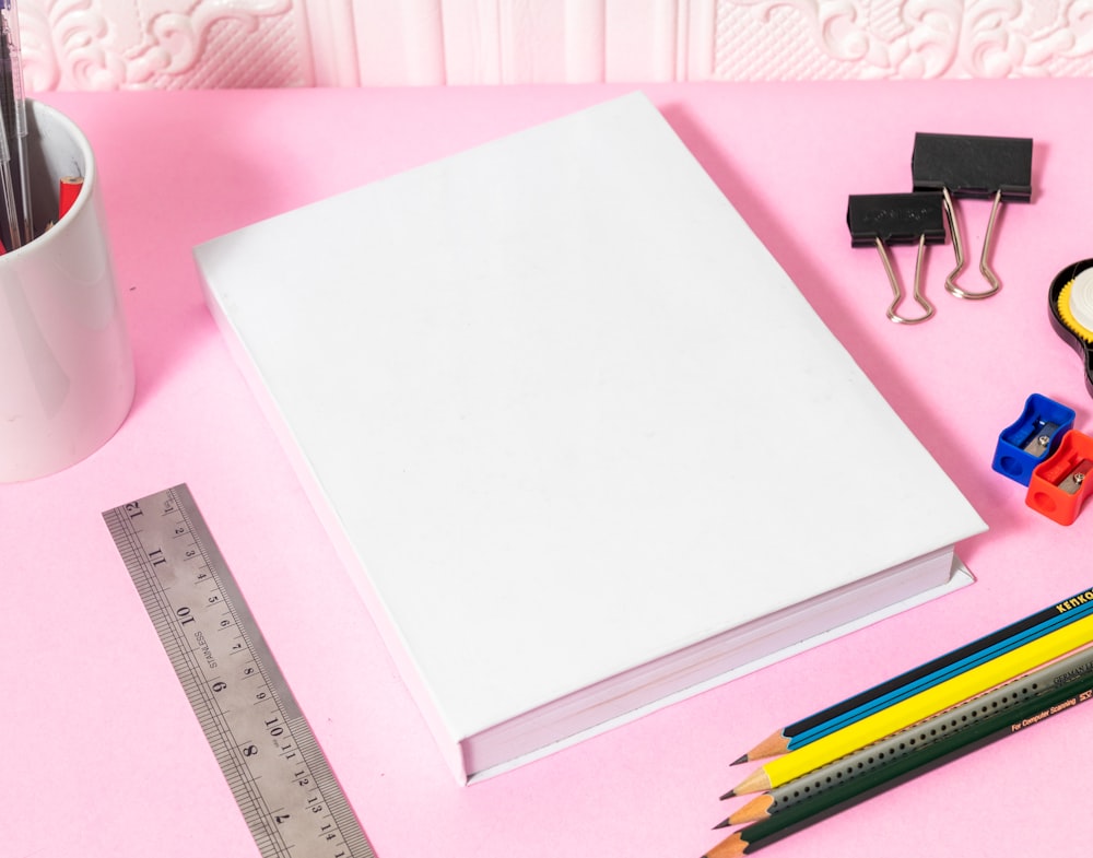 un cuaderno, lápices, regla, cinta adhesiva y lápices en un rosa