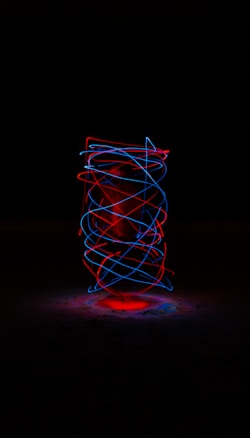 A dark background highlights swirling neon lights in red and blue, creating a dynamic spiral pattern. The lights loop around a central, glowing core, giving a sense of motion and energy.