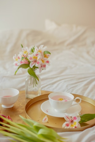 A delicate cup of floral tea surrounded by fresh blossoms and soft sunlight.
