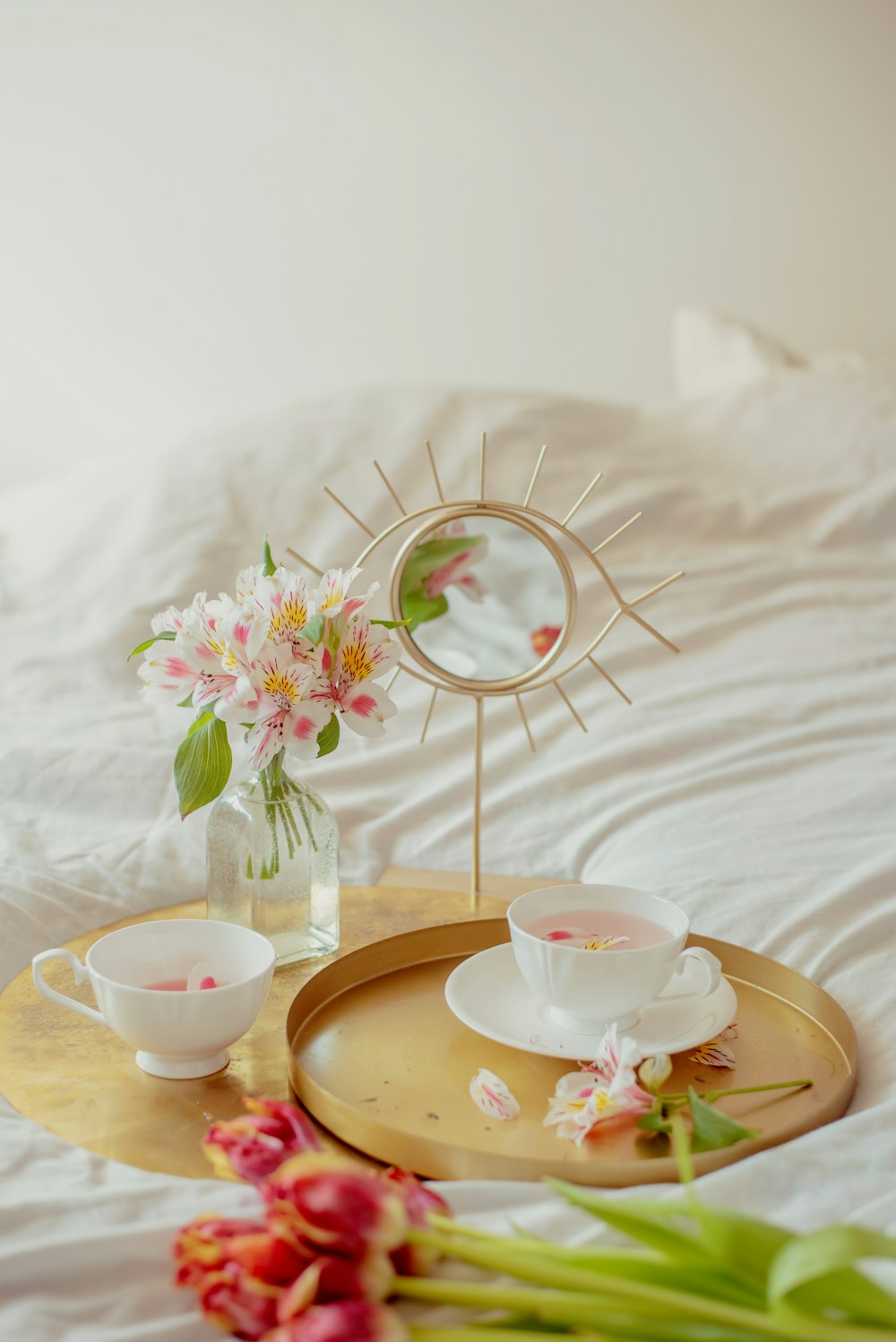 a tray with flowers and a mirror on a bed