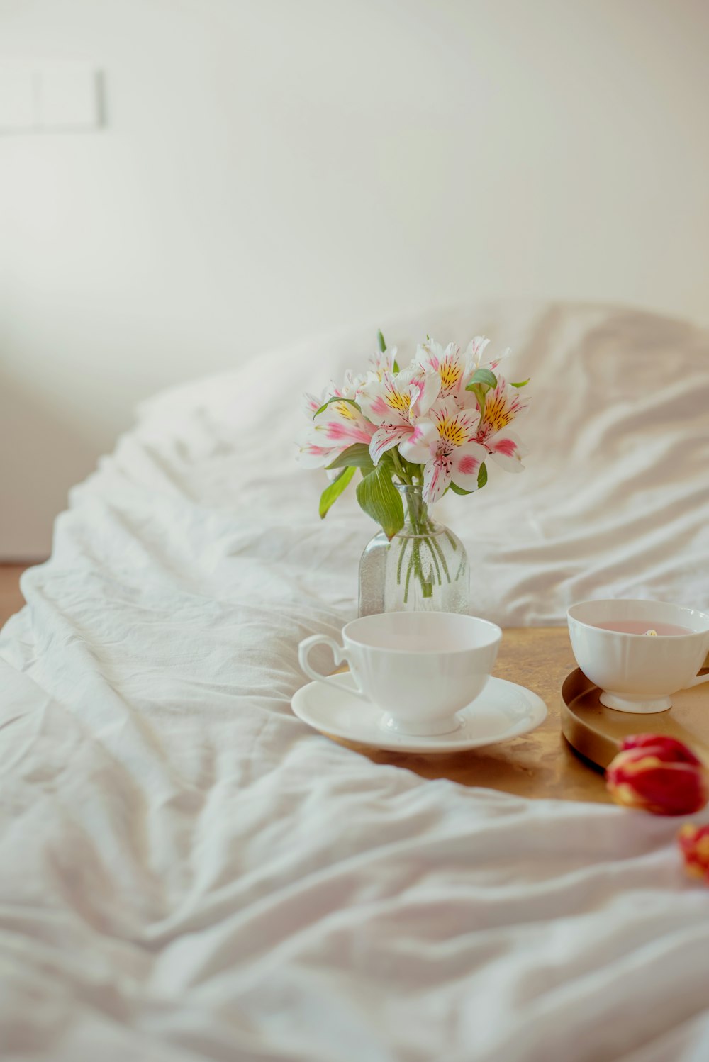 a vase of flowers and two cups on a bed