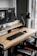 A modern workspace with a large computer monitor displaying 3D modeling software, set on a wooden desk. A keyboard and mouse are placed neatly in front of the monitor. The scene includes a black adjustable desk lamp on the right and a visible computer tower underneath the desk. The workspace is by a window with sheer curtains, allowing natural light to enter.