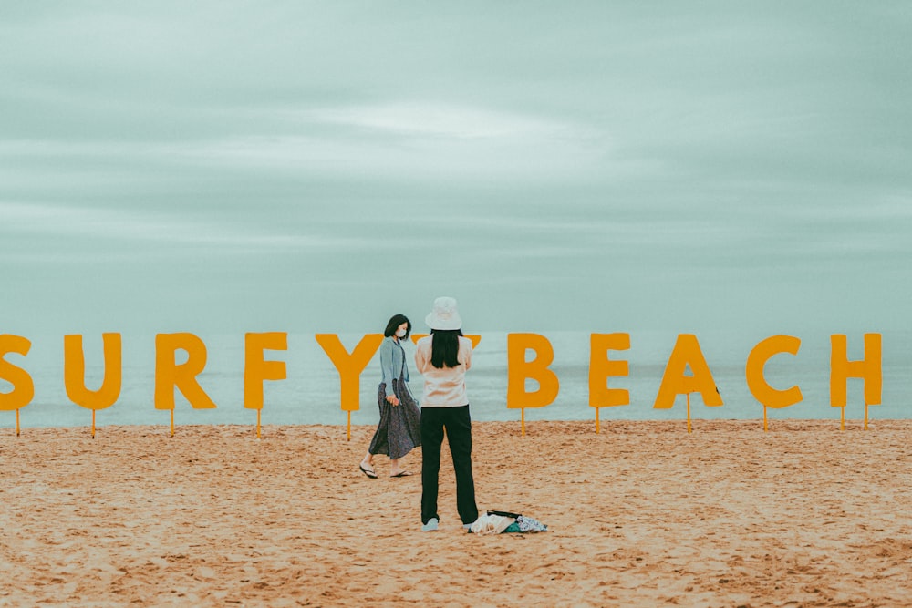 a couple of people standing on top of a sandy beach