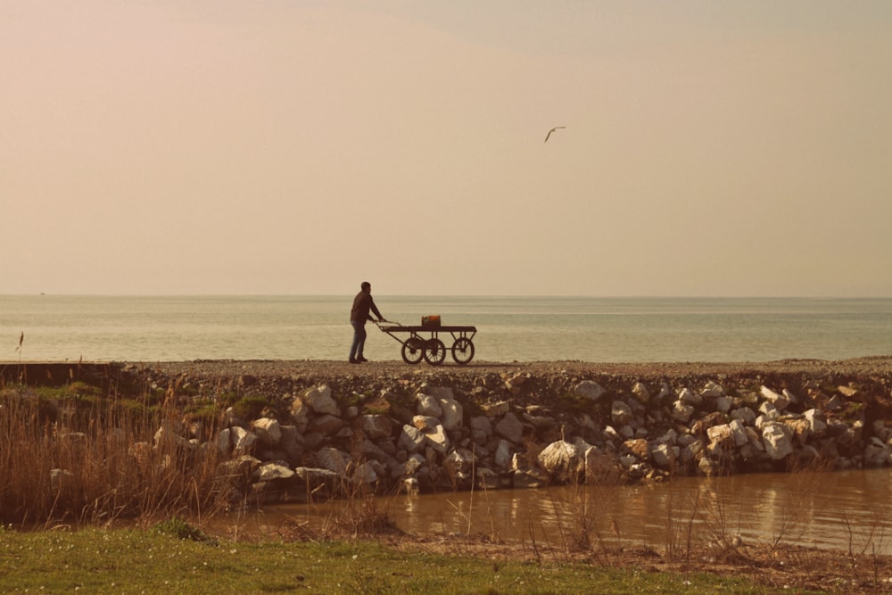 a man pushing a wheelbarrow near a body of water