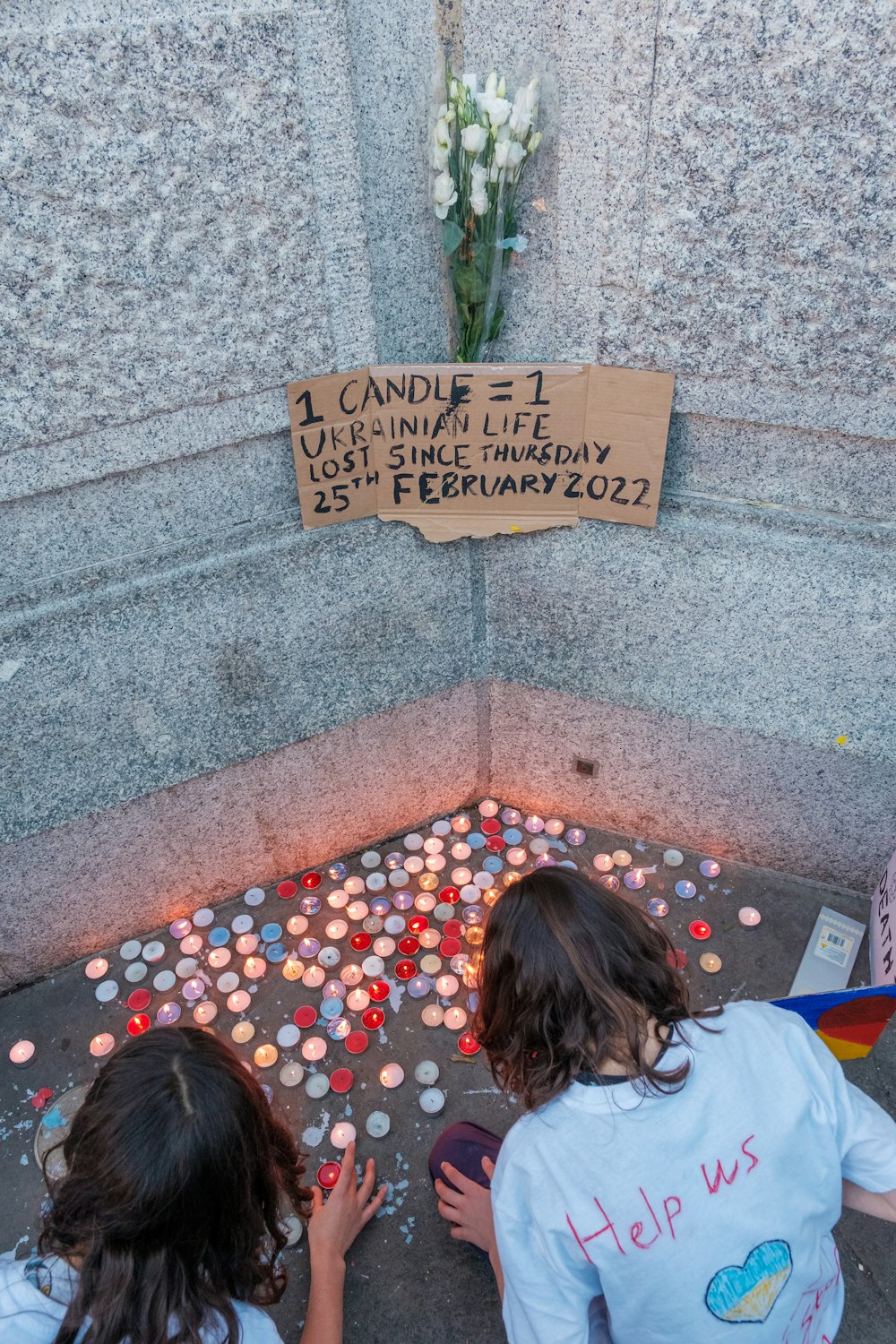 two young girls sitting on the ground in front of a memorial