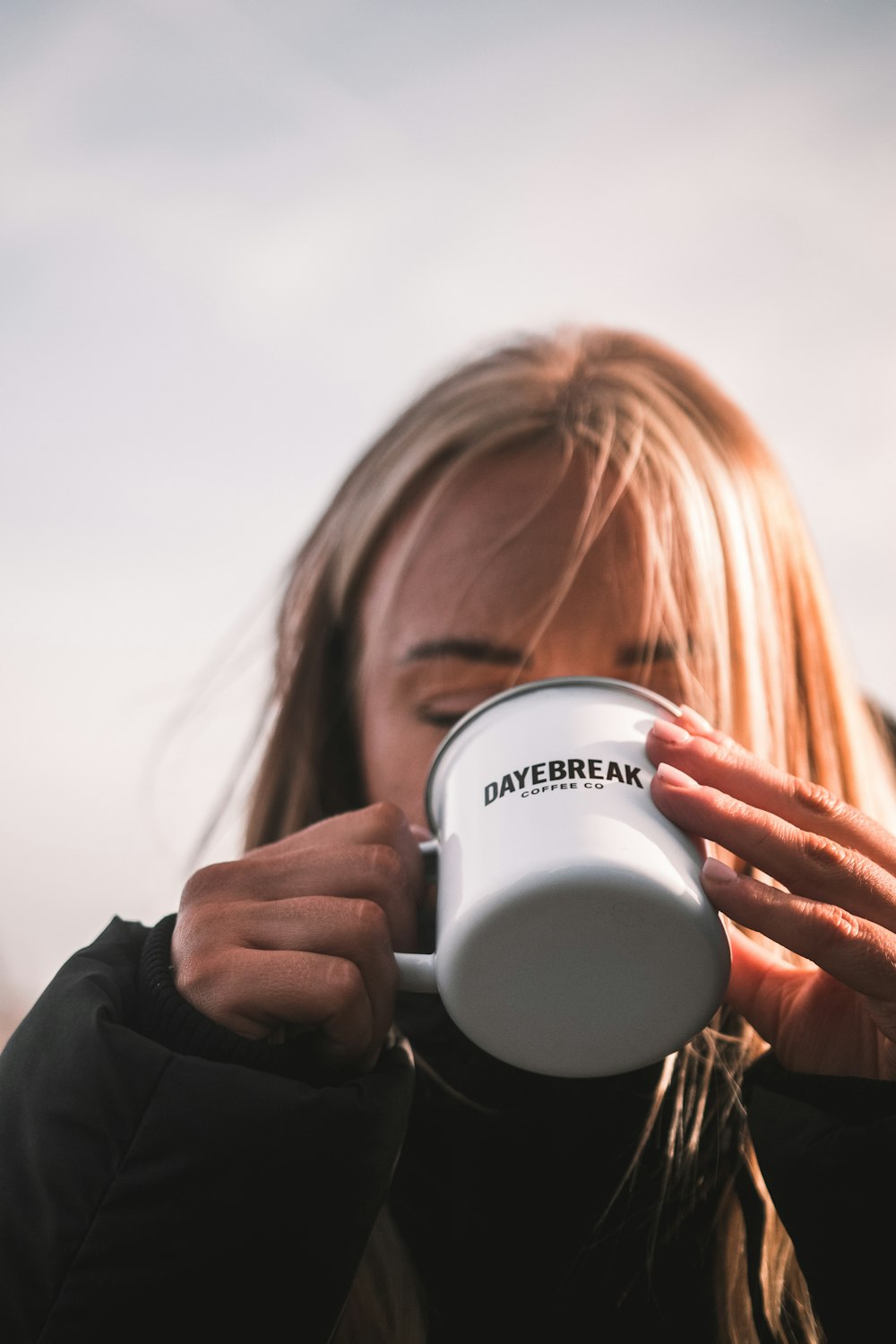 a woman drinking from a white coffee mug