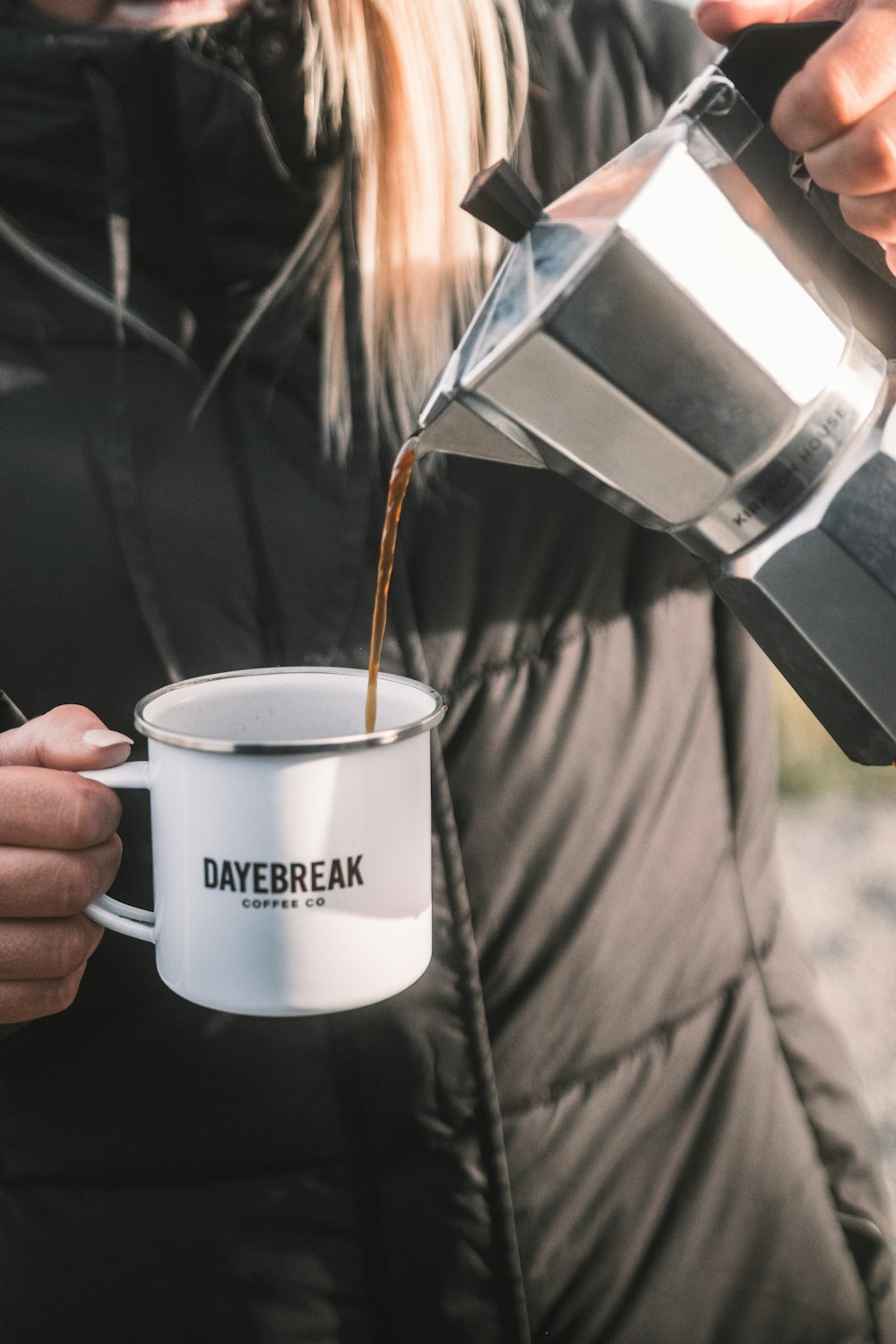 a woman pouring coffee into a white coffee mug