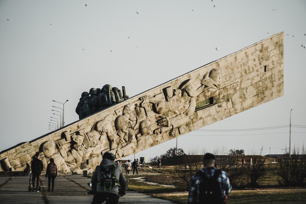a group of people walking past a large stone sculpture