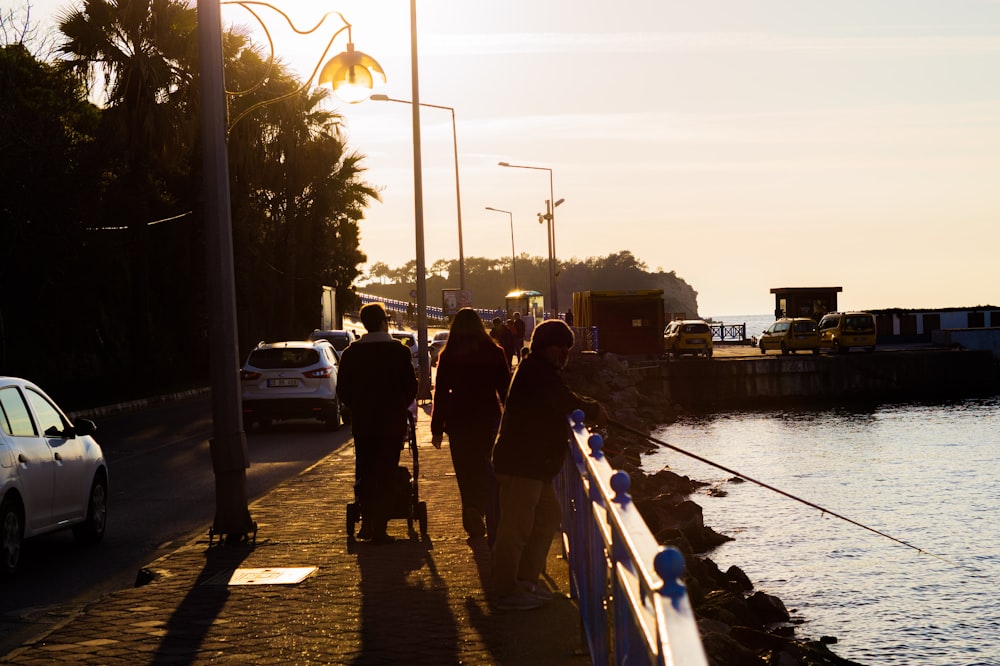 a group of people walking down a sidewalk next to a body of water