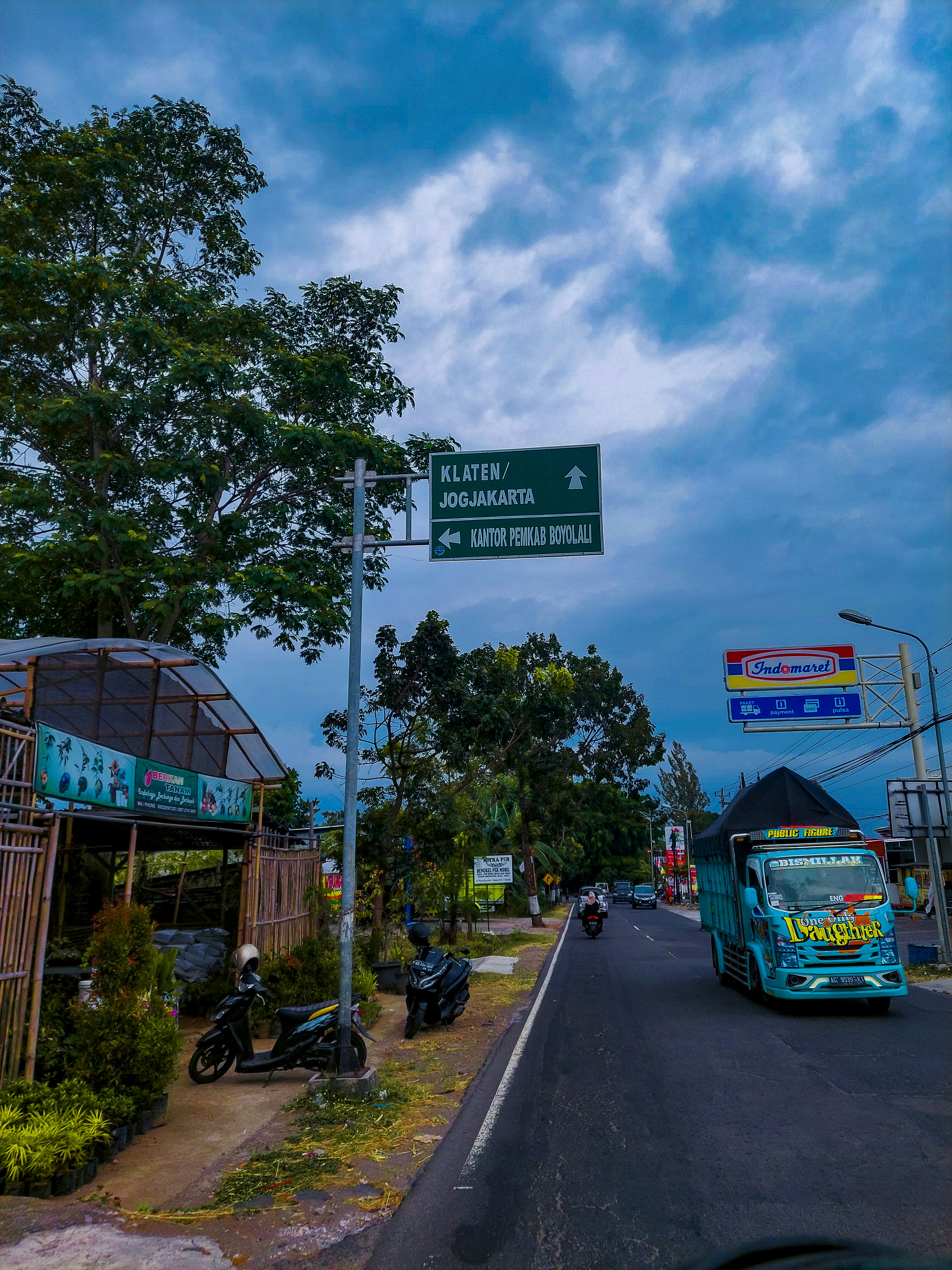 Bus biru melaju di jalan di sebelah hutan hijau rimbun