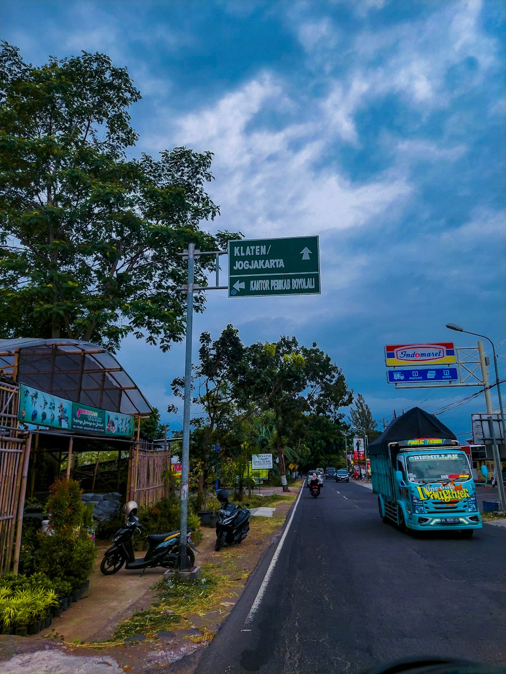 a blue bus driving down a street next to a lush green forest