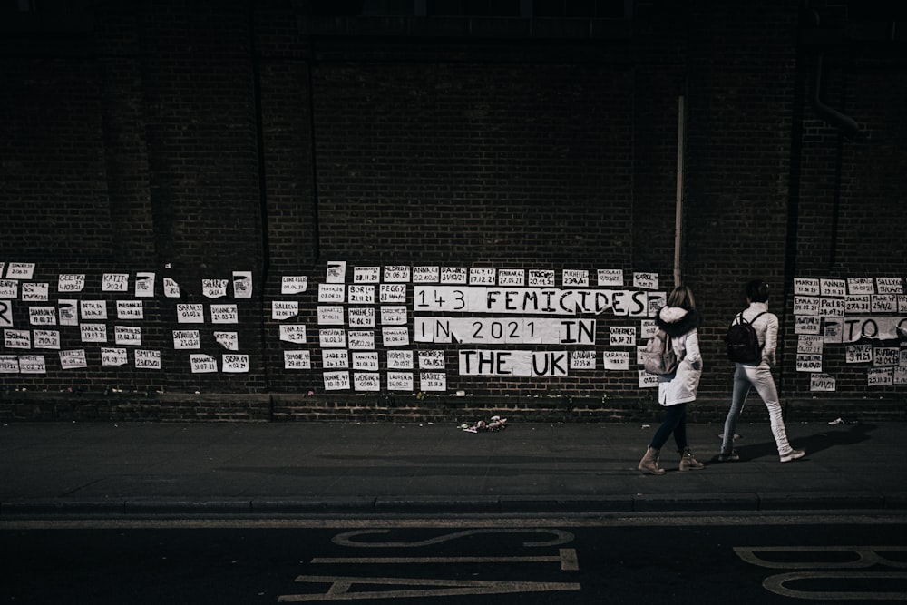 a group of people walking down a street next to a wall