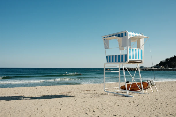 Lifeguard scanning the ocean from a lookout tower with rescue board nearby.