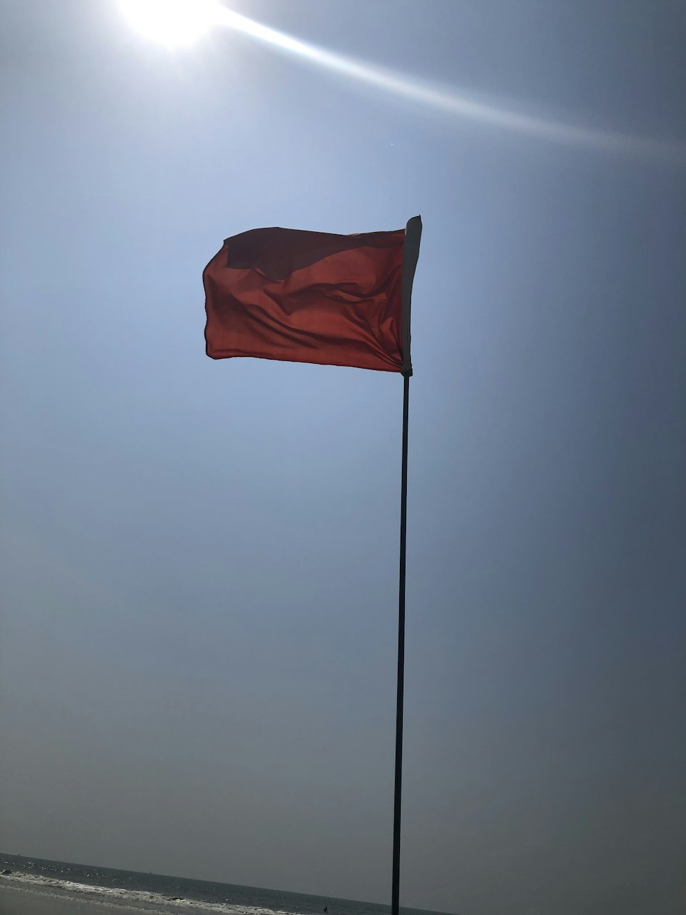 a red flag flying in the wind on a beach