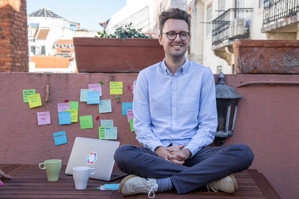 a man sitting on a bench in front of a wall with sticky notes on it