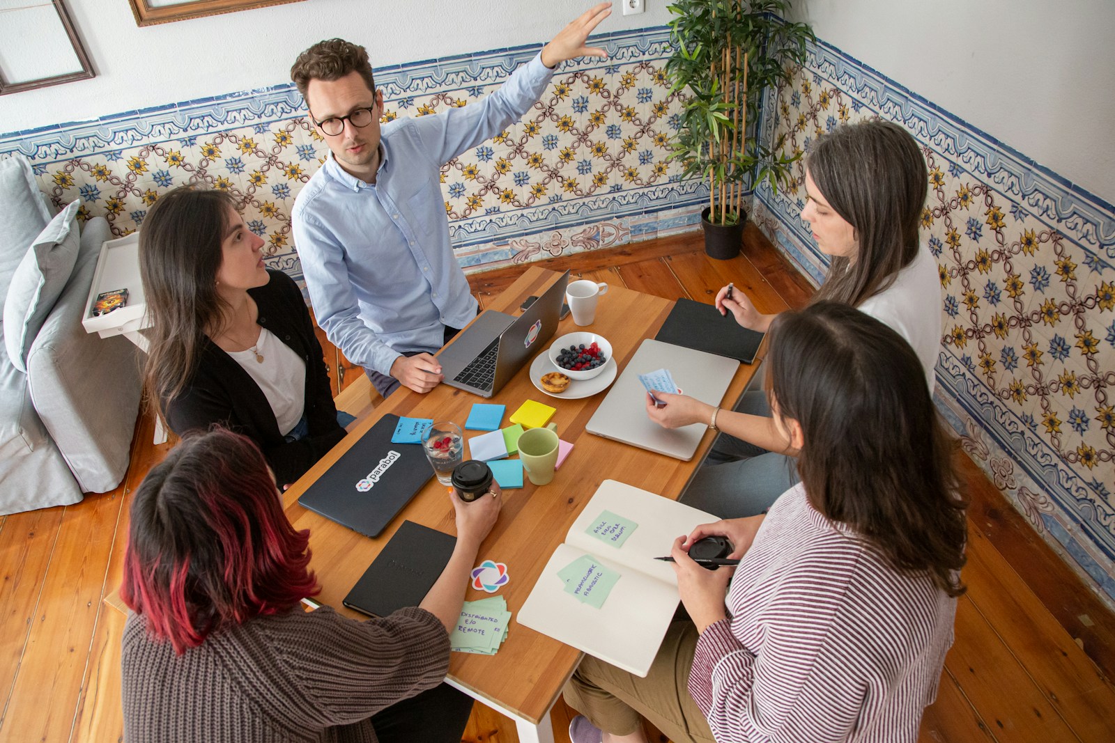 Équipe commerciale de PME B2B en rituel hebdomadaire autour d'une table de réunion avec ordinateur portable et post-its, animateur debout