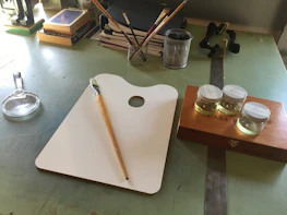 Shot of an artist’s workstation with brushes, paints, and a miniature mid-painting.