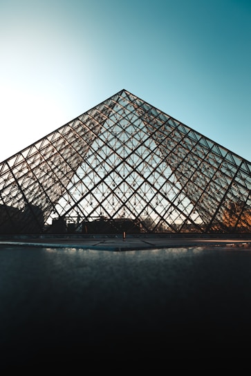 A sleek stainless steel pyramid surrounded by lush greenery and sunlight.