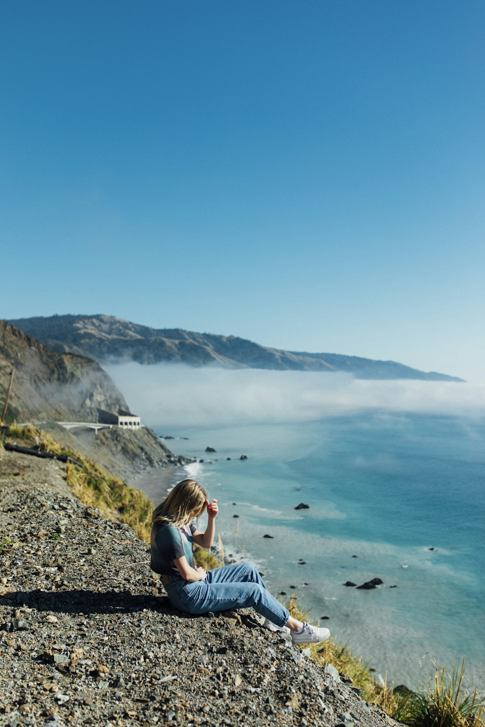 a woman sitting on top of a hill next to the ocean