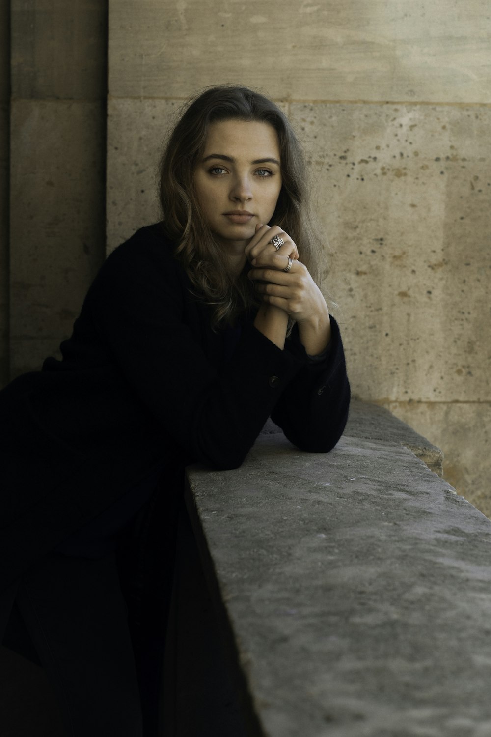 a woman leaning against a wall with her hands on her chin