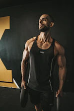 a man in a black tank top holding a barbell