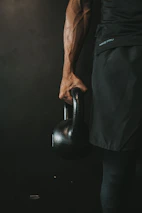Athletic man performing intense workout with kettlebells in a moody studio setting.