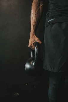 Athletic man performing intense workout with kettlebells in a moody studio setting.